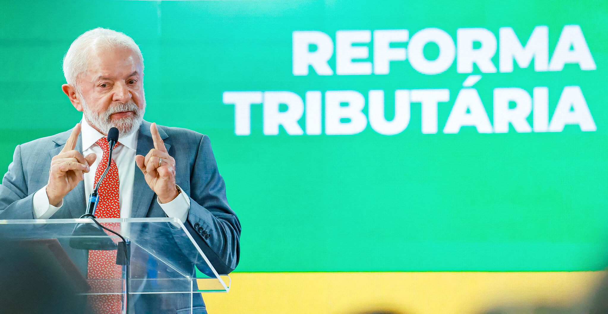 Lula discursa em púlpito diante do telão com o letreiro Reforma Tributária